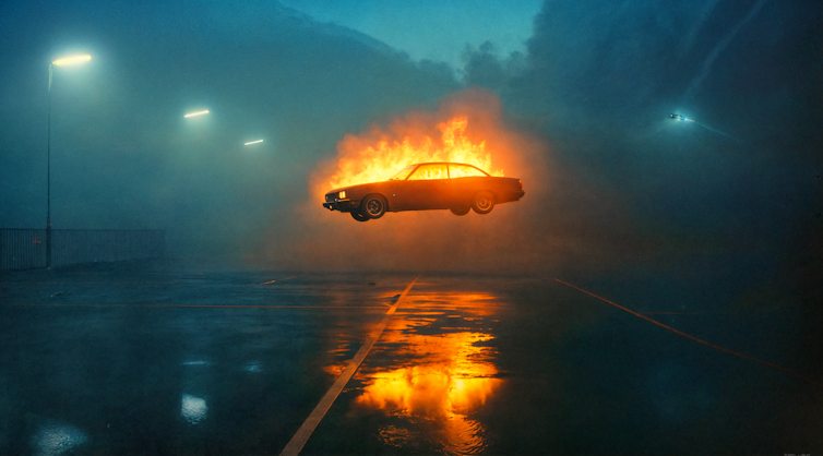 A car in flames mid-air on a foggy night.